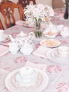 the table is set with pink and white flowers in vases, china dishes, and teacups