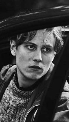 black and white photo of young man in car looking out the window with serious look on his face