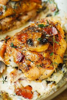 two pieces of chicken covered in sauce and herbs on top of a white plate with mushrooms