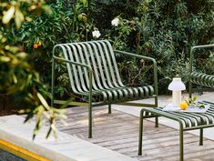 two green chairs sitting next to each other on a wooden deck near bushes and flowers