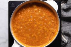 a pot filled with soup sitting on top of a stove next to a towel and spoon