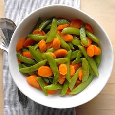 a white bowl filled with carrots and green beans on top of a wooden table