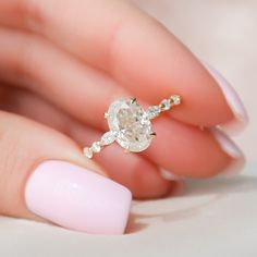 a woman's hand holding a ring with a diamond on it and a pink manicure