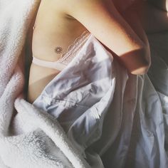 a woman laying in bed under a blanket with her arm wrapped around the edge of her chest