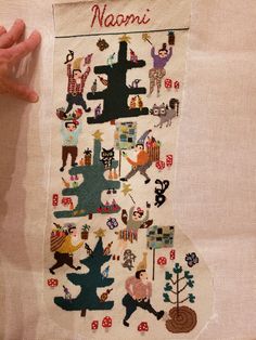 someone is holding up a cross stitch christmas stocking with images of people and animals on it