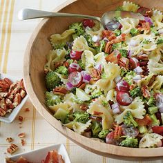 a wooden bowl filled with pasta salad next to two bowls of nuts and other food