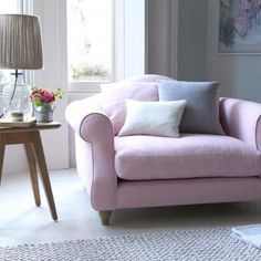 a pink chair sitting in front of a window next to a table with flowers on it