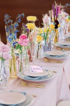 the table is set with flowers in vases, plates and napkins on it