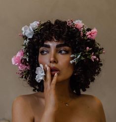 a woman with flowers in her hair is holding her hand to her mouth and looking at the camera