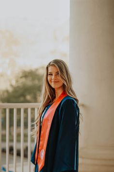 a woman standing in front of a pillar wearing an orange and blue graduation robe