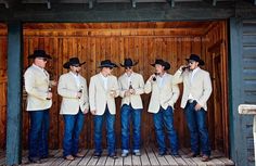 a group of men standing next to each other in front of a wooden wall wearing cowboy hats