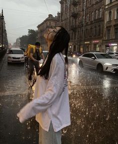 a woman is standing in the rain with an umbrella over her head and looking at cars