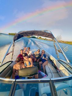 a group of people riding on the back of a boat under a rainbow filled sky