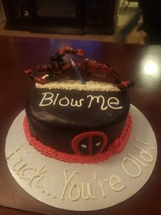 a birthday cake with the words blow me and deadpool on it, sitting on top of a table