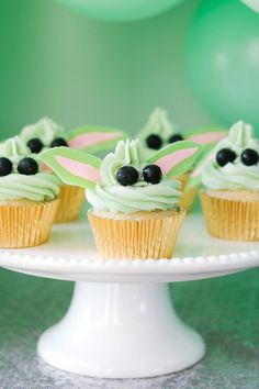 some cupcakes with green frosting and black berries on top are sitting on a cake plate