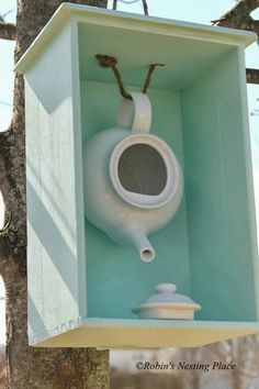 a white birdhouse with a blue roof and window on the outside, attached to a tree