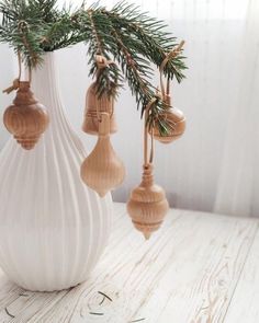 a white vase filled with christmas ornaments on top of a wooden table next to a pine tree