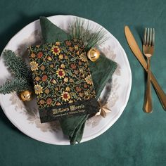 a table setting with napkins and gold utensils on a green cloth covered plate