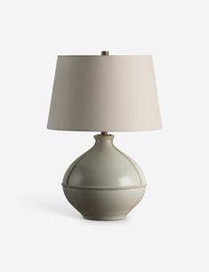 a white table lamp with a beige shade on the base and a light bulb attached to it