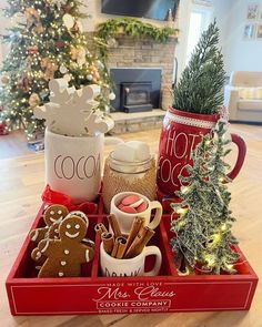 a tray filled with cookies and mugs on top of a wooden table next to a christmas tree