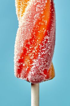 an orange and white lollipop with sugar on top against a blue sky background