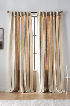 a white chair sitting next to a window with curtains on top of it and a rug in front of the window