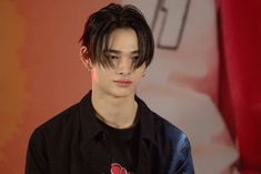 a young man with black hair and piercings on his head standing in front of a red curtain