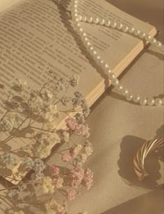 an open book with pearls and flowers on it next to a string of bracelets