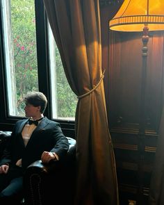 a man in a tuxedo sitting next to a window with a lamp on it