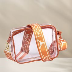 Now Trending! Enhance your game day ensemble with our newest clear purse, complete with two interchangeable strap sets. Effortlessly alternate your style with the choice of matching vegan leather or our chic new patterned shoulder straps. Perfect for UT Austin college football game days! Fall in love with the details: Constructed from transparent vinyl and supple vegan leather, adorned with sophisticated brass hardware accents Confirmed stadium-approved dimensions: 8" x 6" x 2" Includes two adju Clear Stadium Bag, Desert Bloom, Ut Austin, Stadium Bag, College Game Days, Clear Purses, Easy Style, Clear Bag, Texas Longhorns