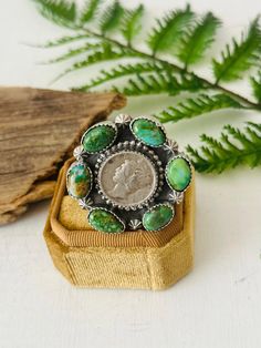 a coin sitting on top of a wooden box next to a fern branch and green leaves