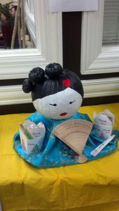 a doll sitting on top of a table next to a fan and other items in front of a window