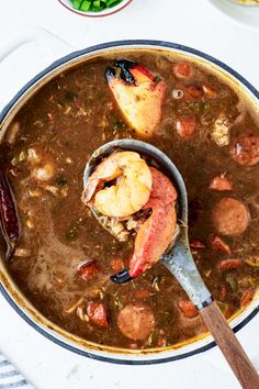 a large pot filled with stew and shrimp on top of a white tablecloth next to bowls of vegetables