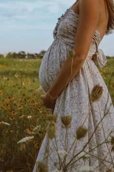 a pregnant woman in a dress standing in a field with wildflowers and blue sky