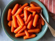 a bowl full of baby carrots with a spoon next to it on a table