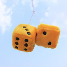 two fuzzy dices hanging from a string in the air with blue sky and clouds behind them