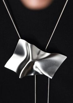 You can't be shy wearing a necklace like this. In fact, this isn't a necklace, it's a statement. Featuring a single large ray pendant with a smooth ripple surface, the undulating metal mimics the movement of waves on the ocean. The pendant hangs flat against the body on a lariat chain that allows it to be worn high, as a choker, or low on the chain. The chain is adjustable with two silicone spacers and crimp beads. 12K Gold plated brass 1 mm 12K Gold brass plated snake chain 31.5" long chain Pen Modern Silver Lariat Necklace As Gift, Modern Metal Lariat Necklace, Dramatic Style, On The Ocean, Crimp Beads, Body On, The Movement, Gold Brass, Lariat Necklace