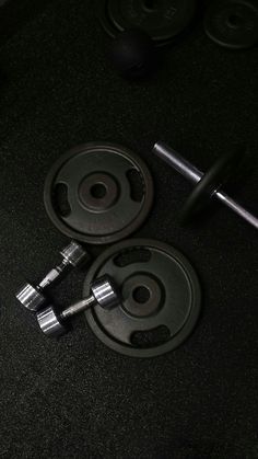 two black dumbbells are sitting next to each other on the floor in front of a barbell