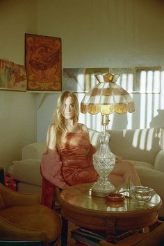 a woman sitting on top of a couch in front of a table with a lamp