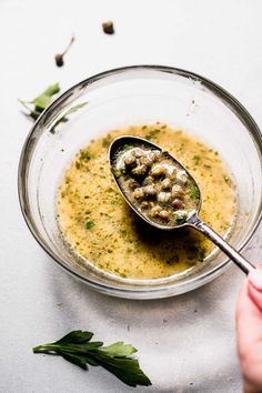 a spoon with some food in it on top of a table next to herbs and leaves