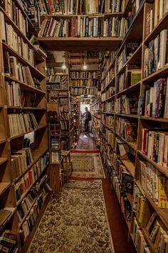 a narrow bookshelf filled with lots of books and people in the distance walking through it