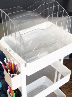 an organized drawer with pens, pencils and markers on the bottom shelf in front of a computer desk