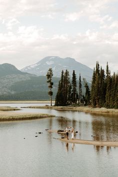 two people standing in the middle of a body of water with mountains in the background