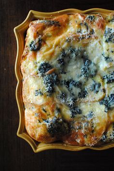 a casserole with cheese and spinach on it in a yellow dish sitting on a wooden table