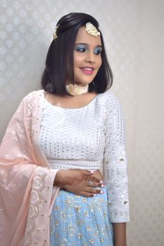 a woman wearing a white top and blue skirt with gold jewelry on her head, standing in front of a wall