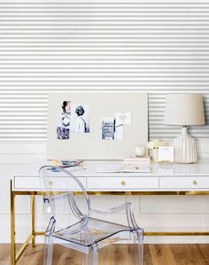 a clear chair sits in front of a white desk with blue striped wallpaper on it