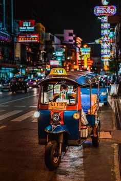 an auto rickshaw is parked on the side of the street in front of neon signs