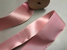 a roll of pink satin ribbon next to a wooden spool