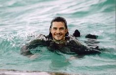 a man swimming in the ocean with his head above the water's surface and smiling at the camera