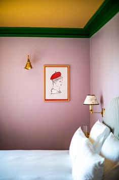 a bedroom with pink walls and green trim on the headboard, white bedding, and framed artwork